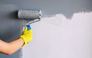 Hand in yellow glove painting wall in gray color with a roller brush- how to apply multiple coats of paint